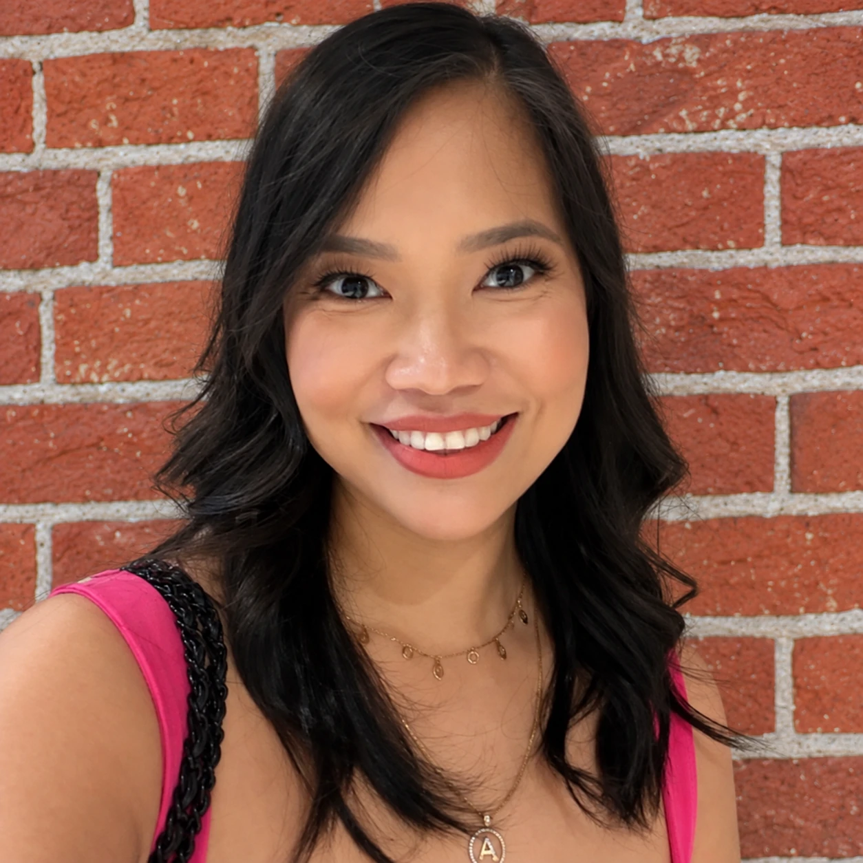Anna Aborro T. smiling in a bright pink top beside a red brick wall